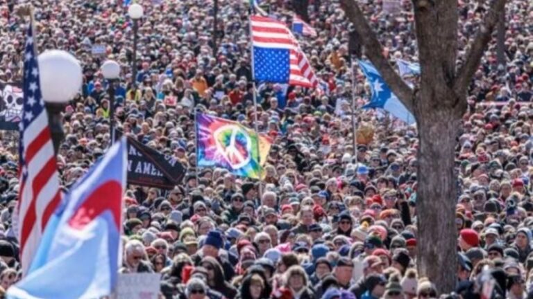 Multitudinaria marcha de protesta en una calle principal de una ciudad estadounidense, con carteles y banderas.