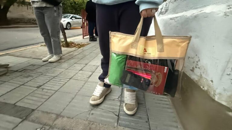Estudiantes ingresando a una escuela con bolsas transparentes en sus manos.