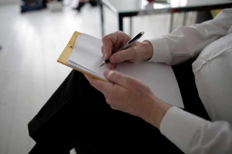 Persona escribiendo una lista de compras en una hoja de papel con un lápiz